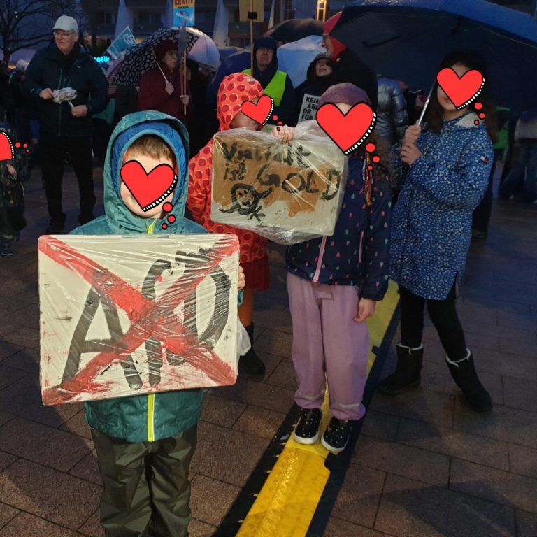 Kinder mit Demoschild. Gesicht durch Herz unkenntlich.